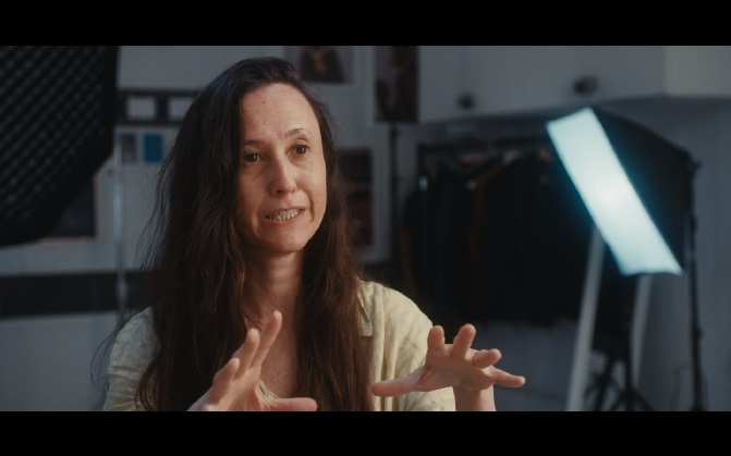 Dark-haired woman in a photography studio talking to someone off-screen.